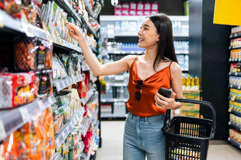 ヴィーガンの加工食品をスーパーの棚から選ぶ女性の写真